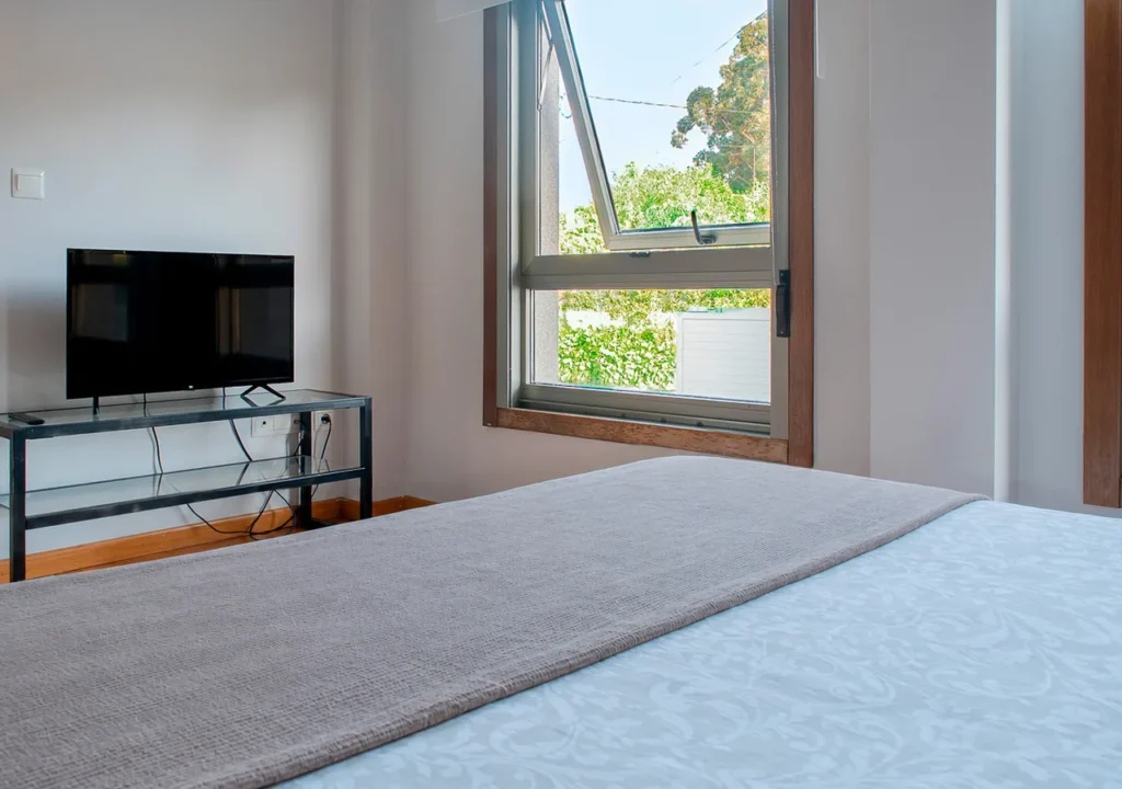 Dormitorio con cama de matrimonio, televisión y ventana en O Igrexario Vacacional
