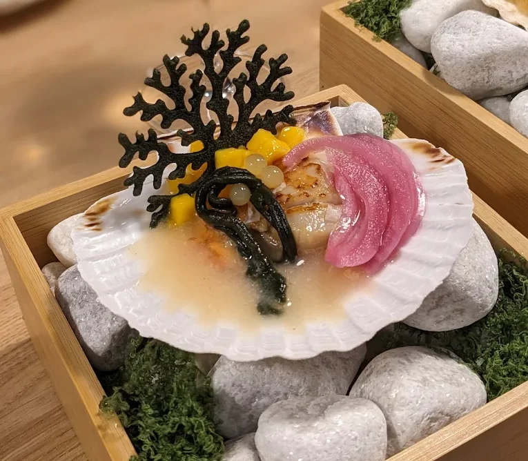 Plato de marisco presentado en una concha con cebolla encurtida y elementos decorativos
