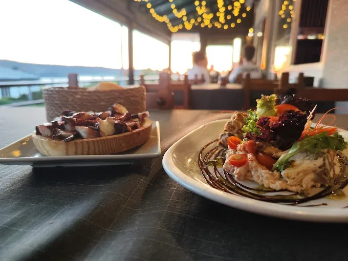 Dos platos de cocina elaborada servidos en Kunkos Restaurante con la ría de Aldán al fondo