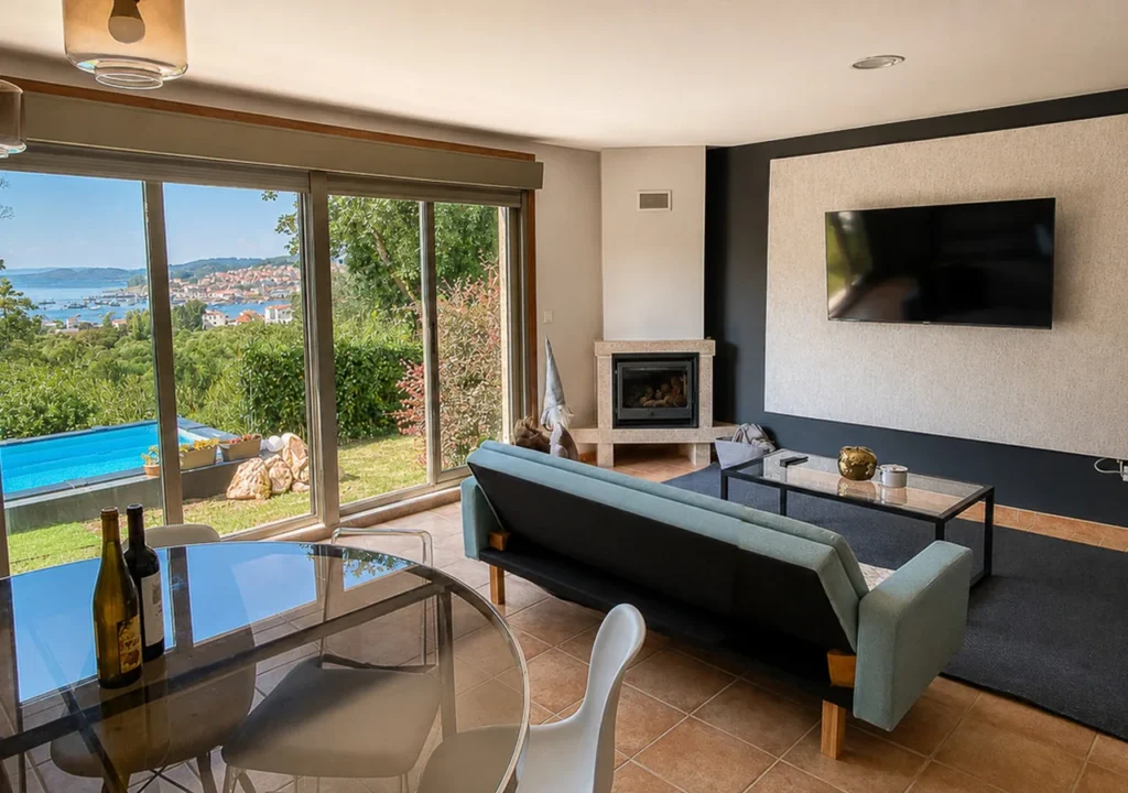 Salón con chimenea, televisión y ventanales con vistas a la ría de Aldán en O Igrexario Vacacional